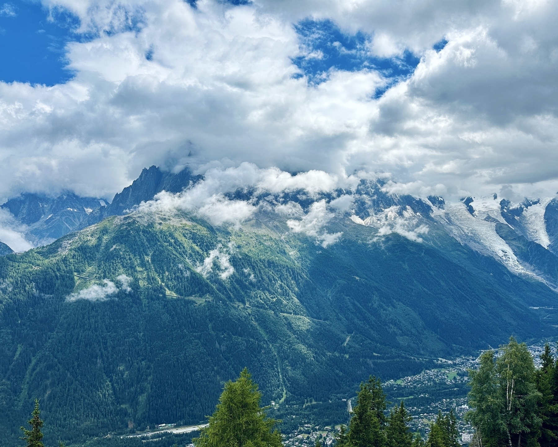 A picturesque mountain range is partially shrouded in clouds, with lush green forests and a valley below.